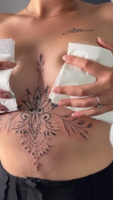 Grand ornement de lotus et de perles tatoué sous la poitrine, prolongé de feuillages.