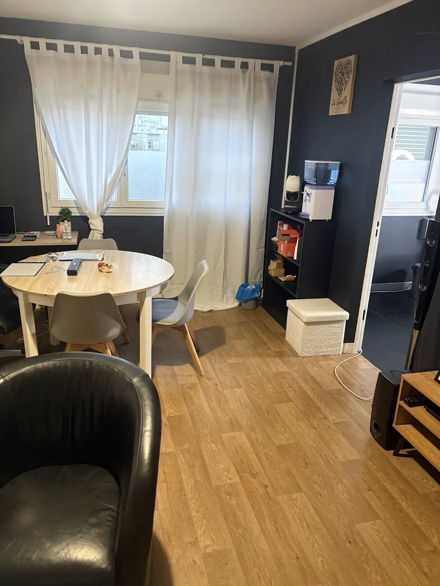 La salle d'accueil du studio, table ronde en bois clair, chaises et fauteuil noir.
